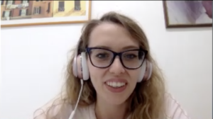 Chiara is a young woman with long wavy blonde hair - she is wearing glasses and headphones and smiling at the camera